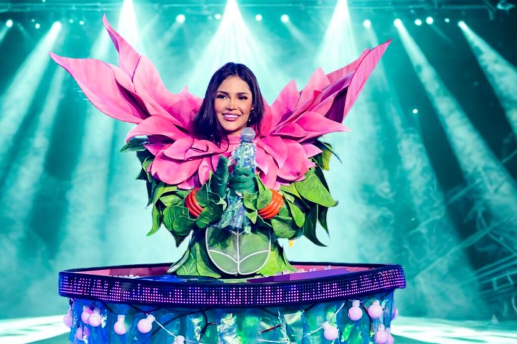 Cantora mascarada com fantasia de flor rosa e verde, revelada no palco de "The Masked Singer Brasil".