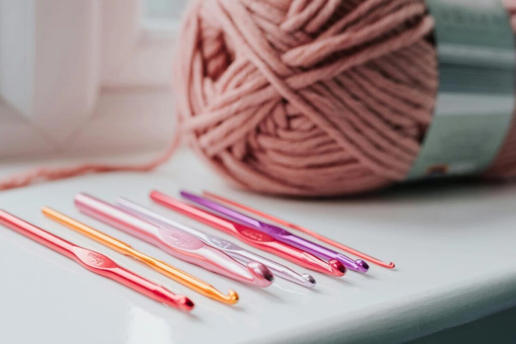 Agulhas de crochê coloridas e novelo de fio rosa